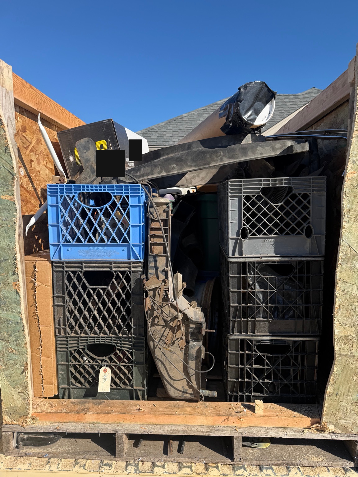 Lower view into the same packed wooden crate, showing stacked plastic crates and a large central assembly with wires and rods. Shipping labels obscured.